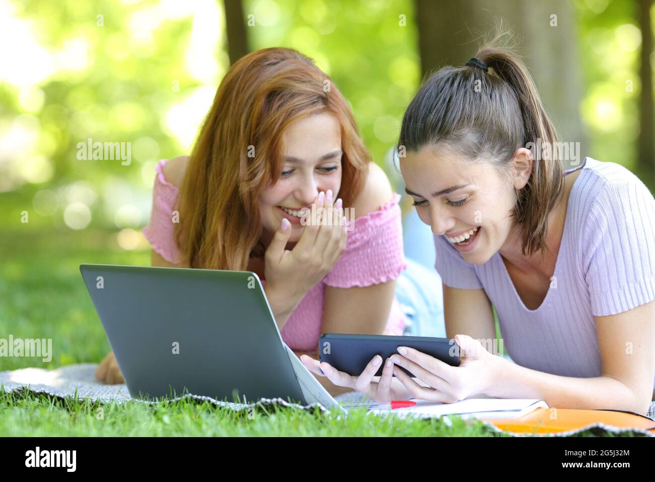 Felici gli studenti che guardano video online su smartphone ridendo e sdraiati sull'erba in un parco Foto Stock
