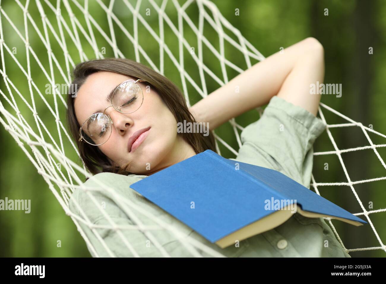 Donna rilassata che dorme sull'amaca con un libro sul petto in una foresta Foto Stock