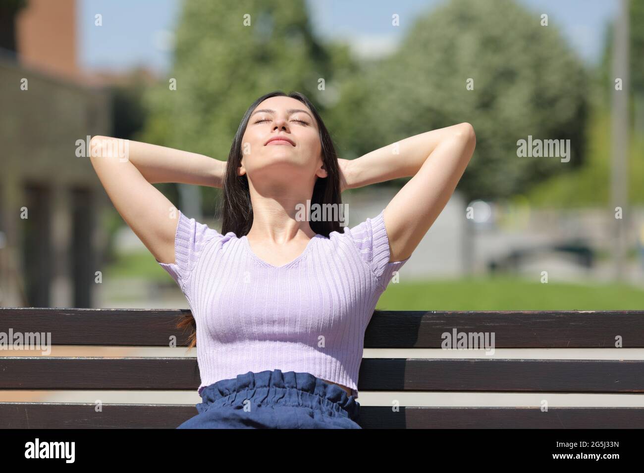 Vista frontale ritratto di una donna mista che si rilassa seduta in una panchina in un parco Foto Stock