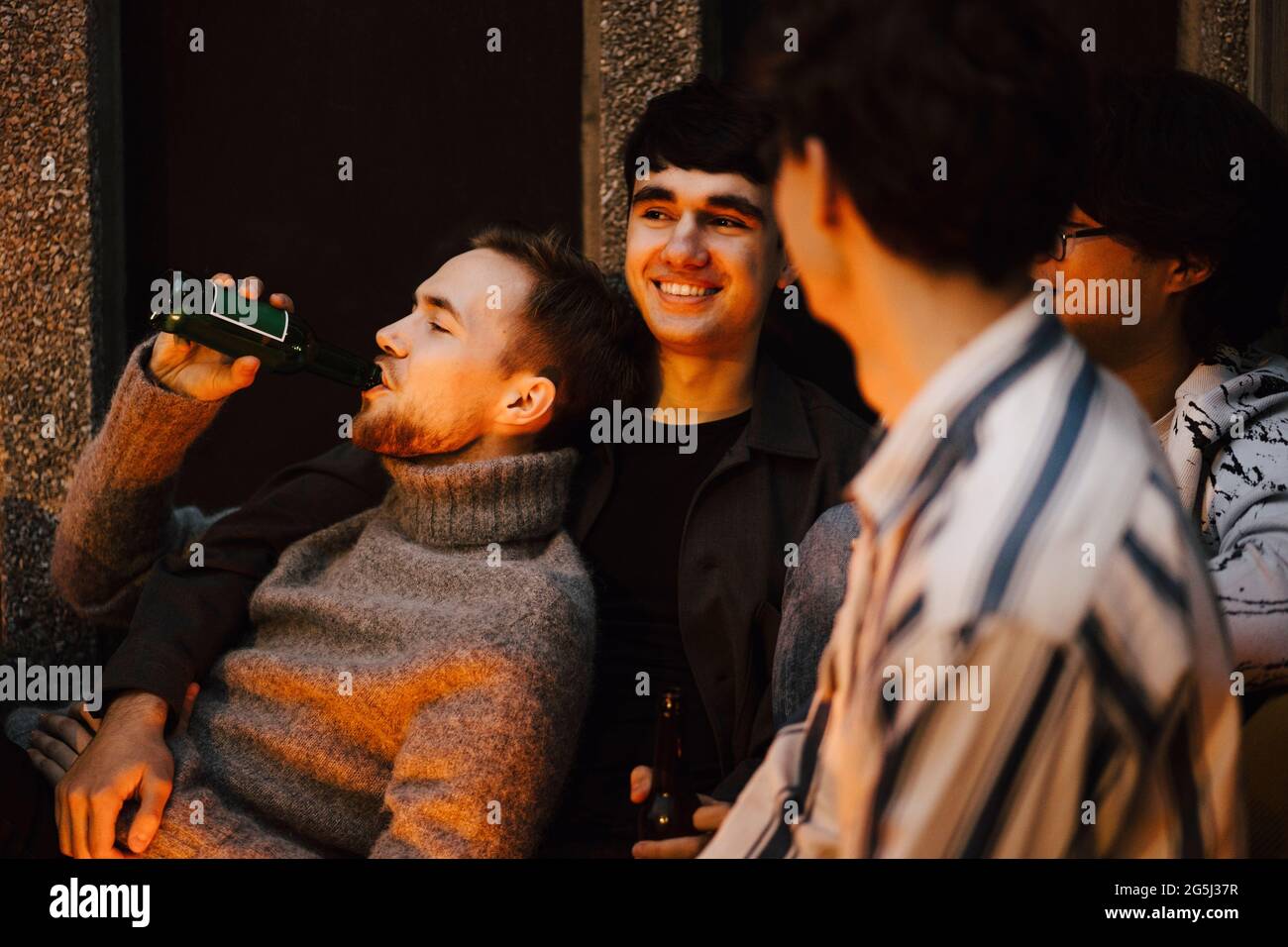Giovane uomo che beve birra mentre si raffredda con gli amici maschi in balcone Foto Stock