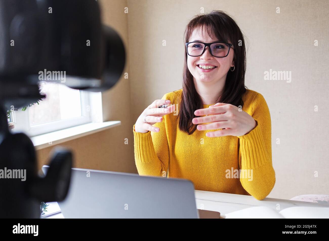 Una ragazza blogger mantiene il suo canale e comunica con gli abbonati attraverso una trasmissione online - UNA giovane donna in un vestito giallo conduce una webina Foto Stock