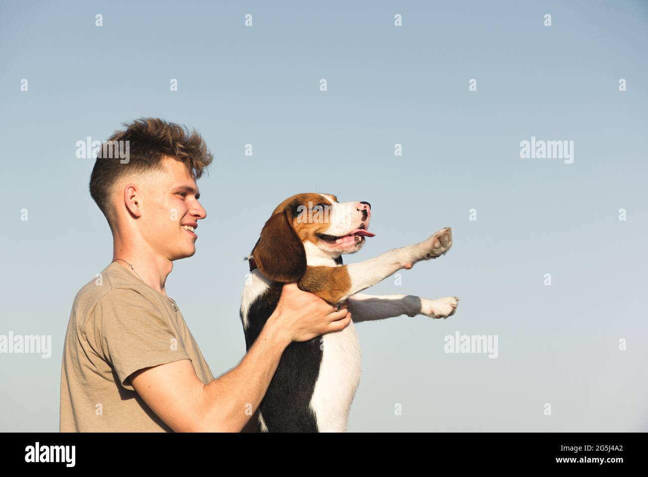Felice giovane uomo tiene il suo cane beagle divertente, sparato contro cielo blu chiaro con spazio copia. Stile di vita con animali domestici, buon proprietario di cucciolo, cane purebred Foto Stock