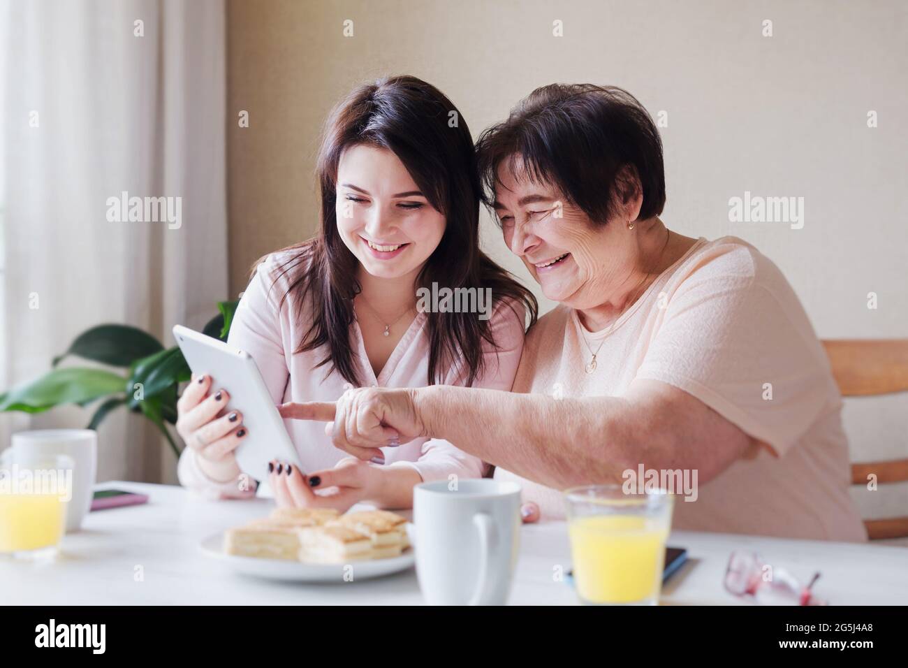 Una madre anziana e una figlia adulta si divertono e guardano una foto o un video su un tablet nei social network - generazioni diverse insieme w Foto Stock