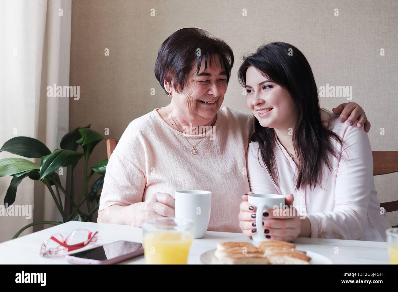 Nonna abbracca amorevolmente sua figlia - i parenti si divertono al tavolo - amici di una donna di diverse età bere tè e chiacchierare - il concetto Foto Stock