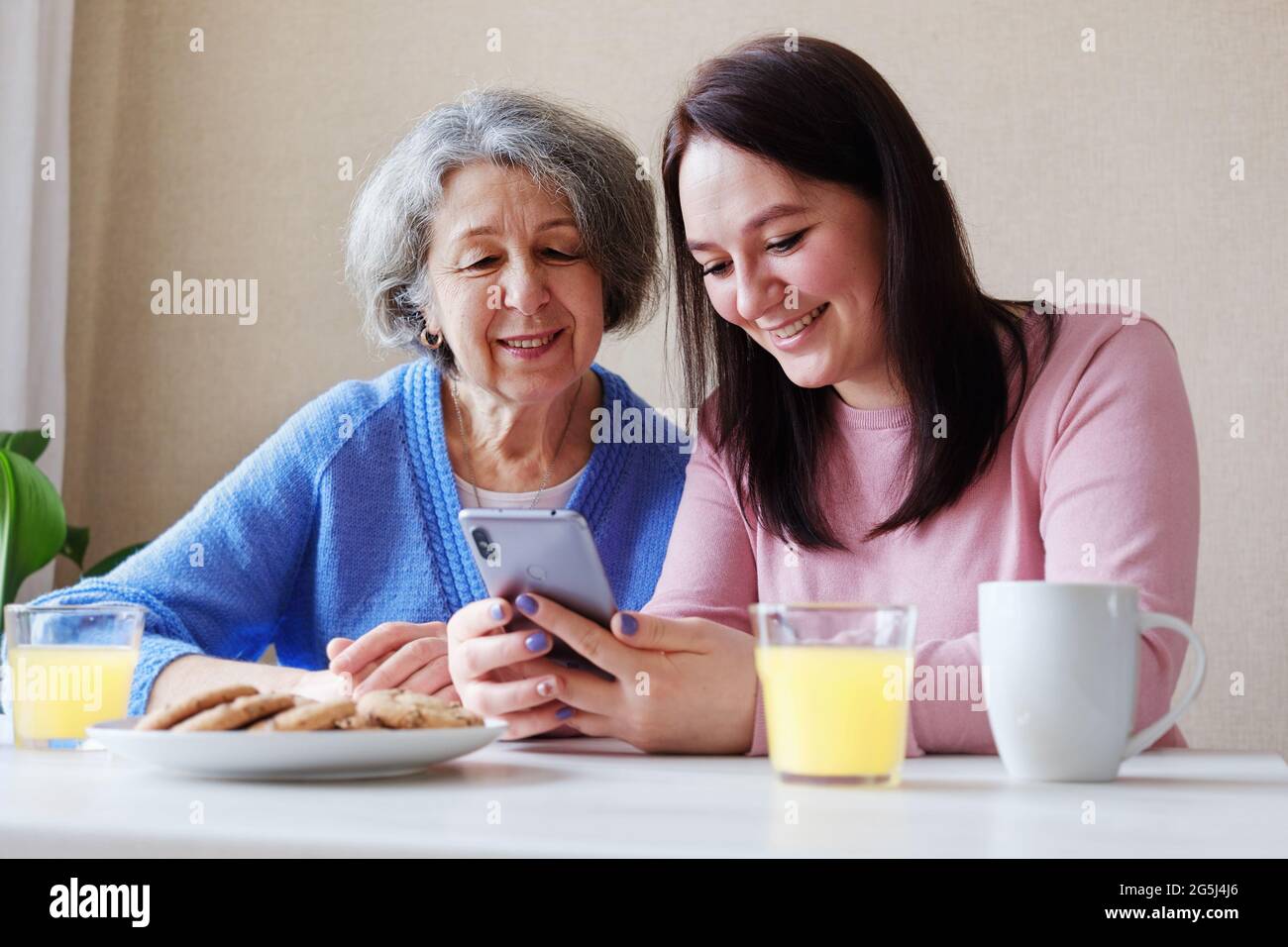 Felice due generazioni di famiglia una madre anziana e una giovane figlia si divertono utilizzando un telefono cellulare per visualizzare i contenuti su Internet - le donne sono Foto Stock