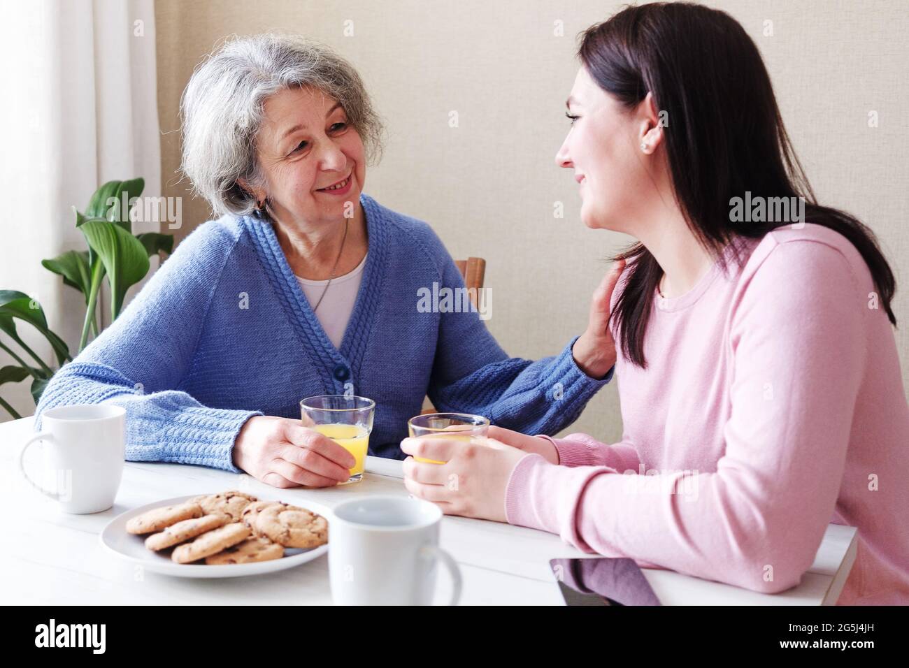 Una figlia visita una madre anziana e parlano insieme a colazione - UNA donna in pensione è visitata da un volontario e parla per mantenere l'healt mentale Foto Stock