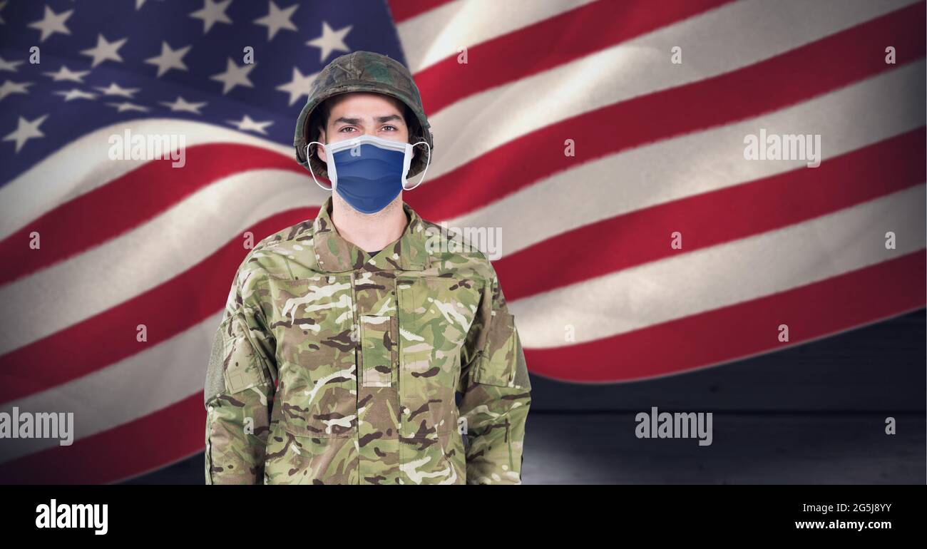 Composizione del soldato che indossa una maschera facciale in piedi all'attenzione, contro l'ondeggiamento della bandiera americana Foto Stock