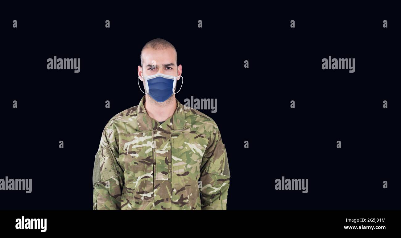 Composizione di un soldato maschio che indossa una maschera facciale, in piedi all'attenzione su sfondo nero Foto Stock