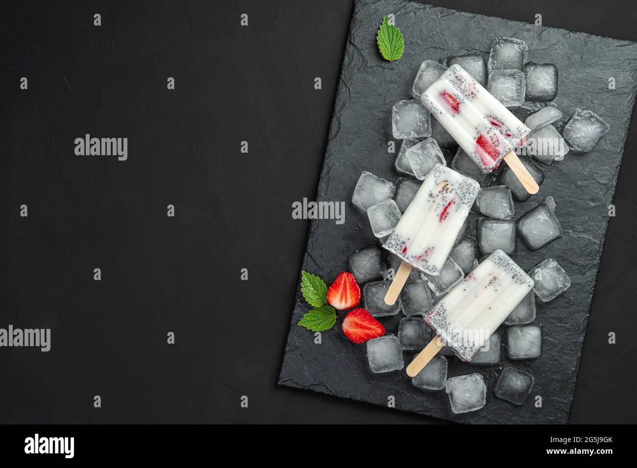 Tre gelati con semi di chia e fragole su un bastone di legno su sfondo nero. Foto Stock