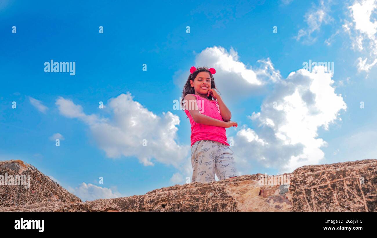 Piccola ragazza gioiosa che si trova su un antico forte vista. Scola girl frontale con stile mood con abito rosa. Foto Stock
