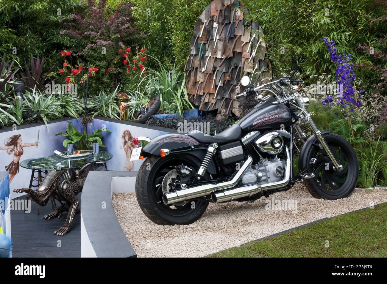 Il giardino sommerso dell'Ace of Spades con pareti dipinte, sculture a spatina, vecchie parti di bicicletta, pneumatici, piante di colore scuro Foto Stock