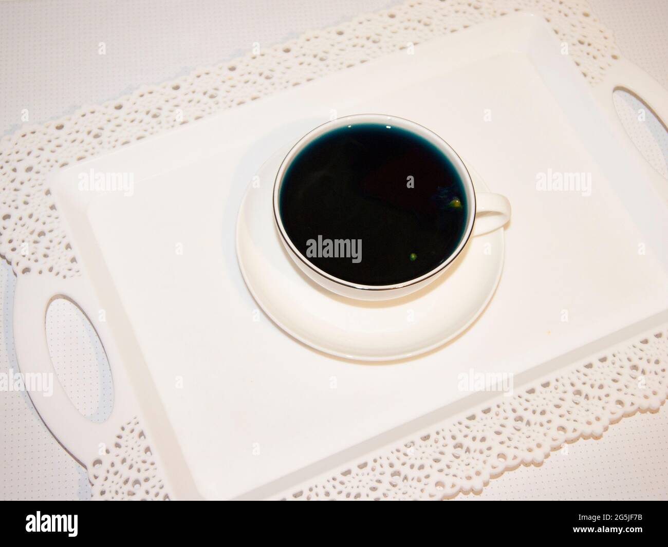 Il colore dell'umore è blu - tè blu in una tazza bianca, che si trova su un piatto bianco e un vassoio bianco bevande utili, proprietà curative. Fitoterapia. Festa del tè. Foto Stock