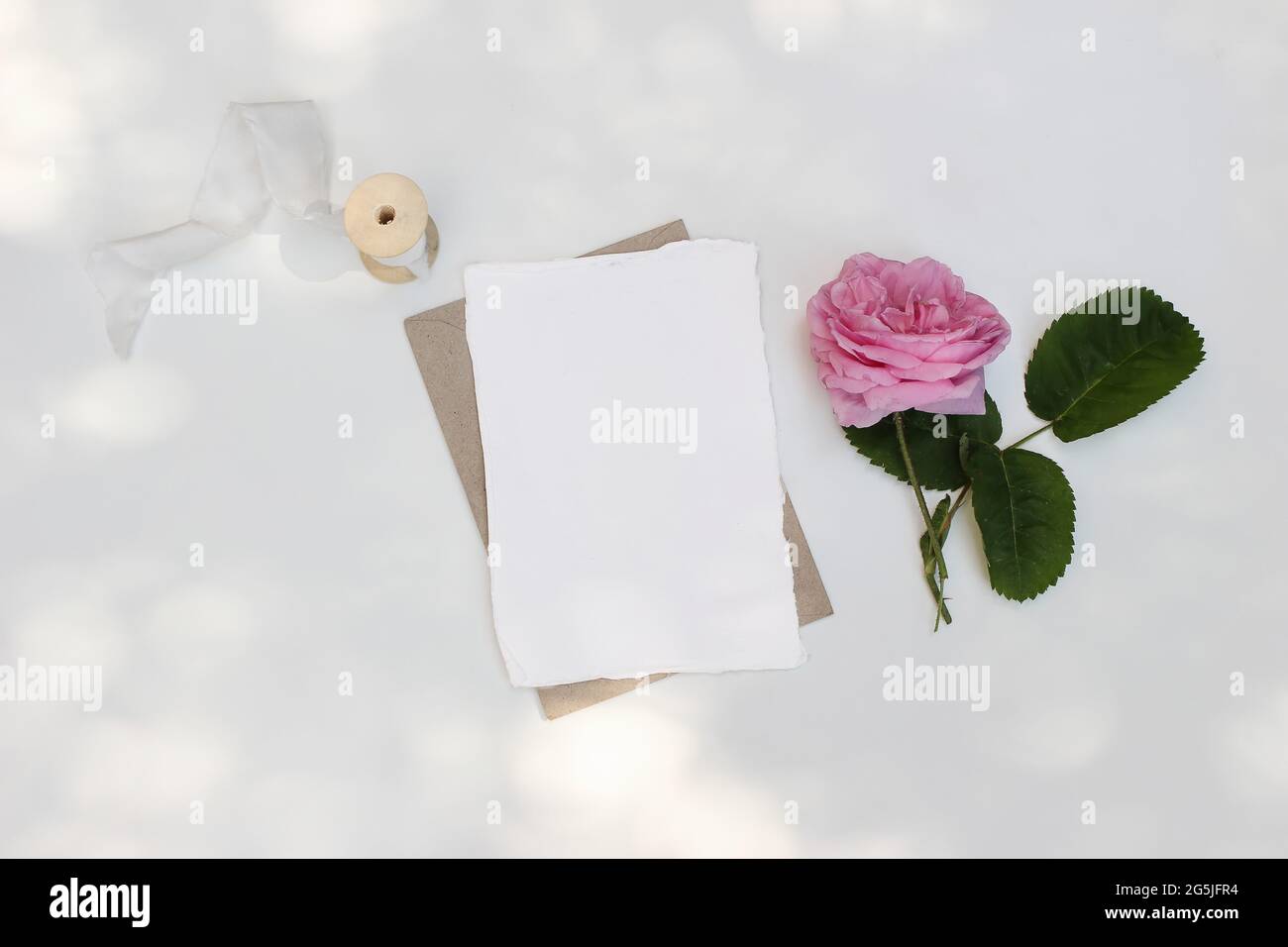 Mock-up di cancelleria per matrimoni estivi. Biglietto d'auguri vuoto, invito con busta artigianale su tavola bianca alla luce del sole. Rosa rosa, rosa Foto Stock