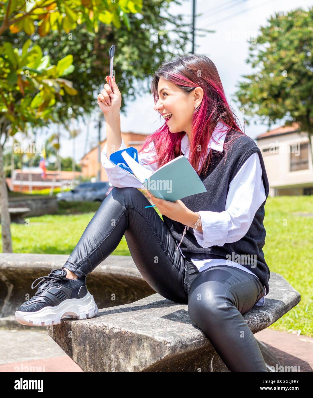 giovane donna seduta in un parco con blocco note per celebrare una buona idea Foto Stock