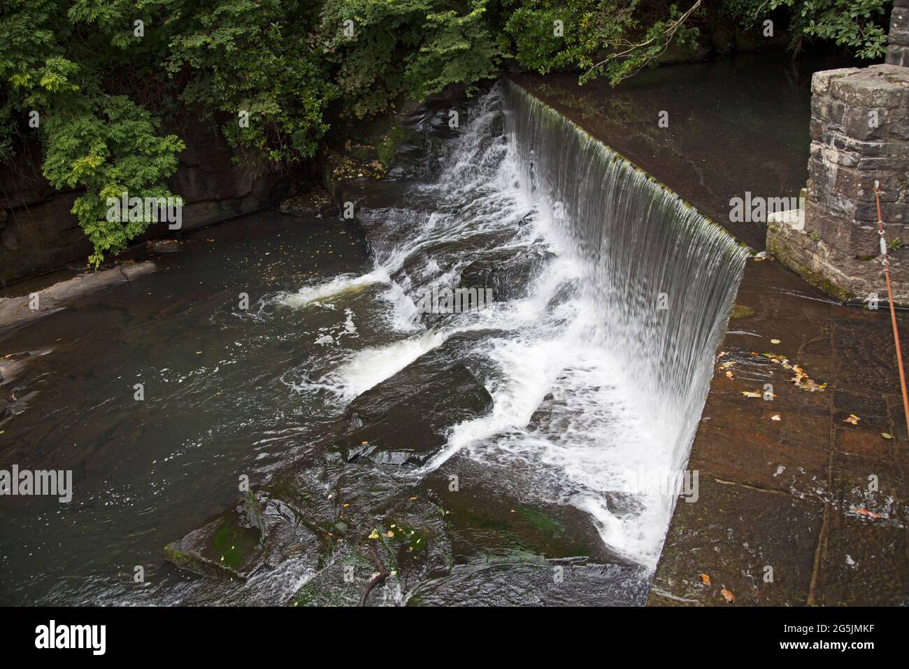 L'acqua che scorre su una cascata di pietra artificiale, o weir, essendo deviata via dal waterwheel di Aberdulais, Neath, Galles Foto Stock