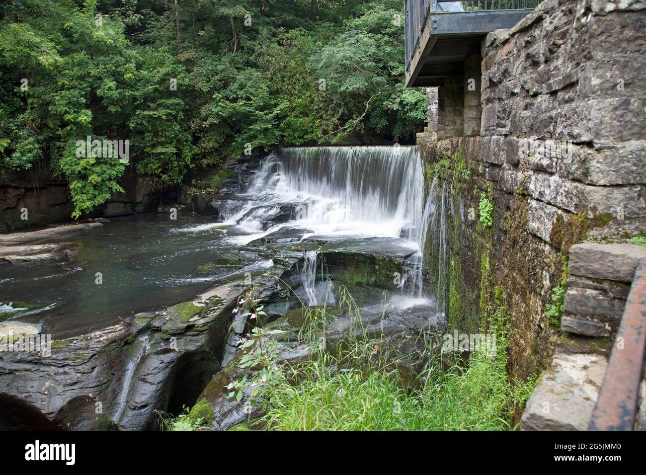 L'acqua che scorre su una cascata di pietra artificiale, o weir, essendo deviata via dal waterwheel di Aberdulais, Neath, Galles Foto Stock