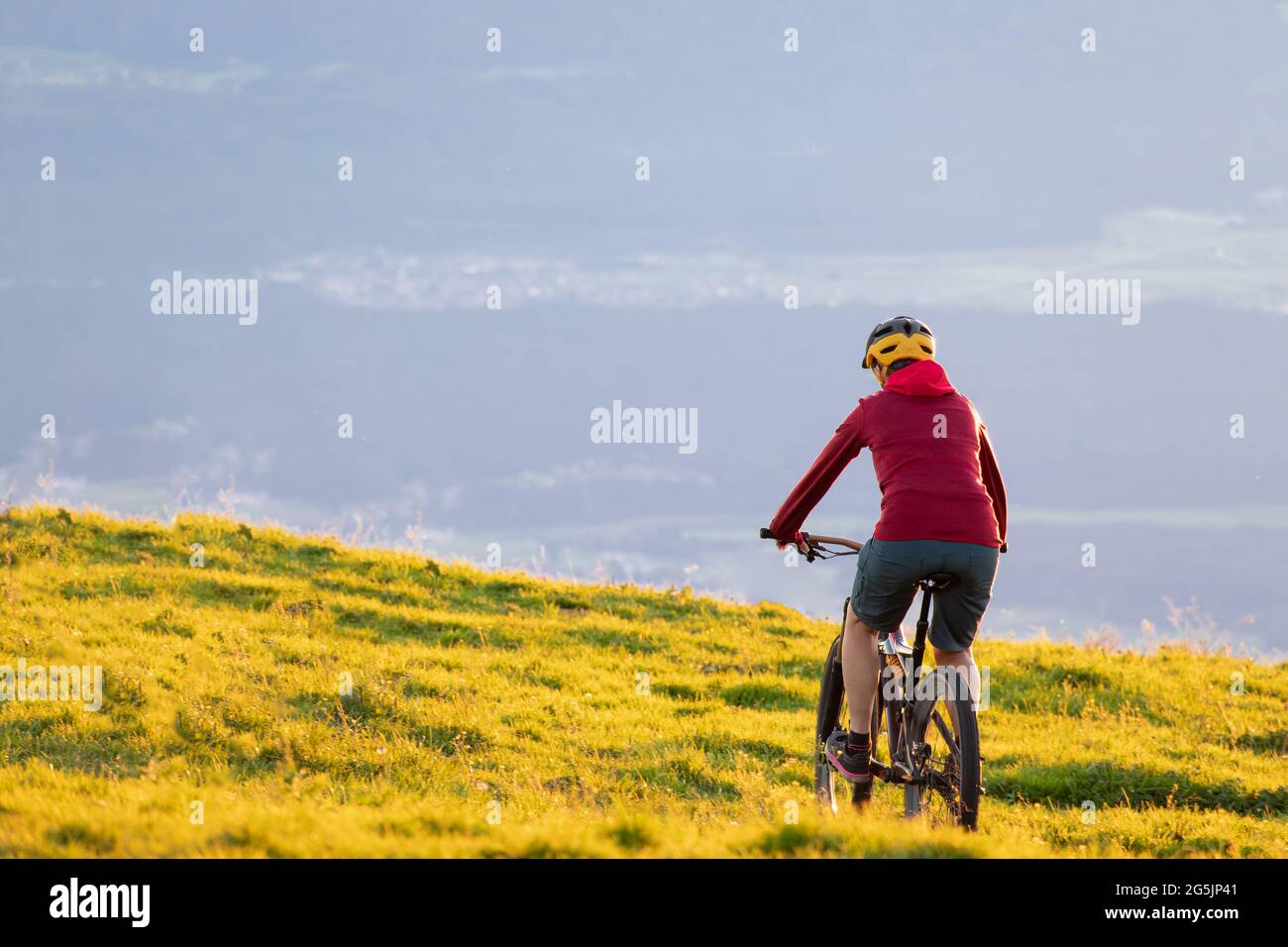 Donna in mountain bike al tramonto. Bella luce dorata estiva. Foto Stock