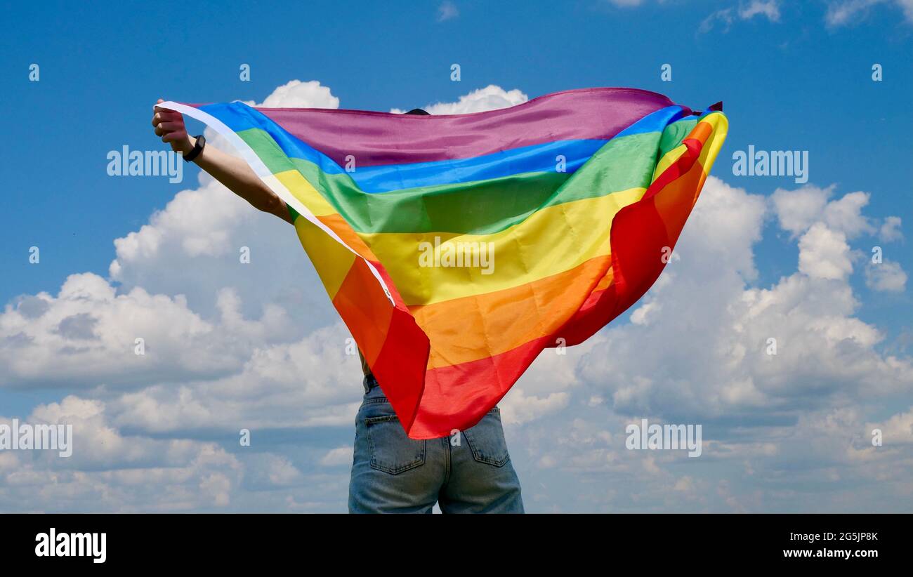 Bisessuale, ragazza, lesbica, donna, transgender, Omosessuale tenendo in mano un arcobaleno LGBT bandiera di identità di genere su sfondo cielo con le nuvole in una giornata di sole e celebrare una parata gay in mese di orgoglio Foto Stock
