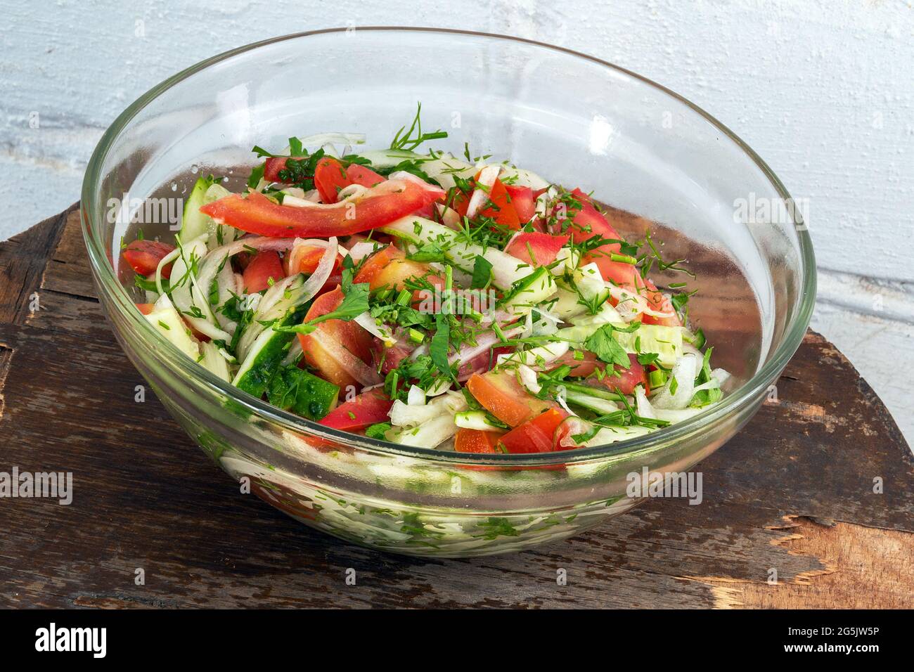 Insalata vegetariana fresca in recipiente di vetro su vecchio tavolo in legno compensato sullo sfondo di una parete di mattoni imbiancati Foto Stock