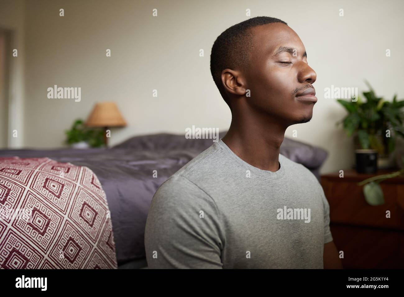Giovane africano meditando con gli occhi chiusi nella sua camera da letto Foto Stock