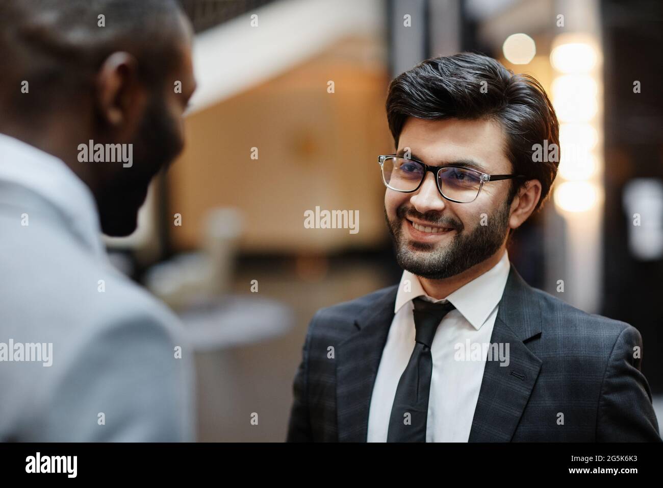 Ritratto di sorridente uomo d'affari mediorientale che parla con il compagno mentre si trova nella hall dell'hotel Foto Stock