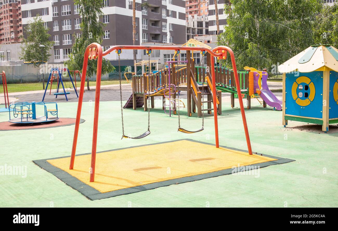 Un colorato e moderno parco giochi nel cortile in un parco senza persone. Swing, carosello esterno per bambini. Un parco giochi in un parco pubblico circondato Foto Stock