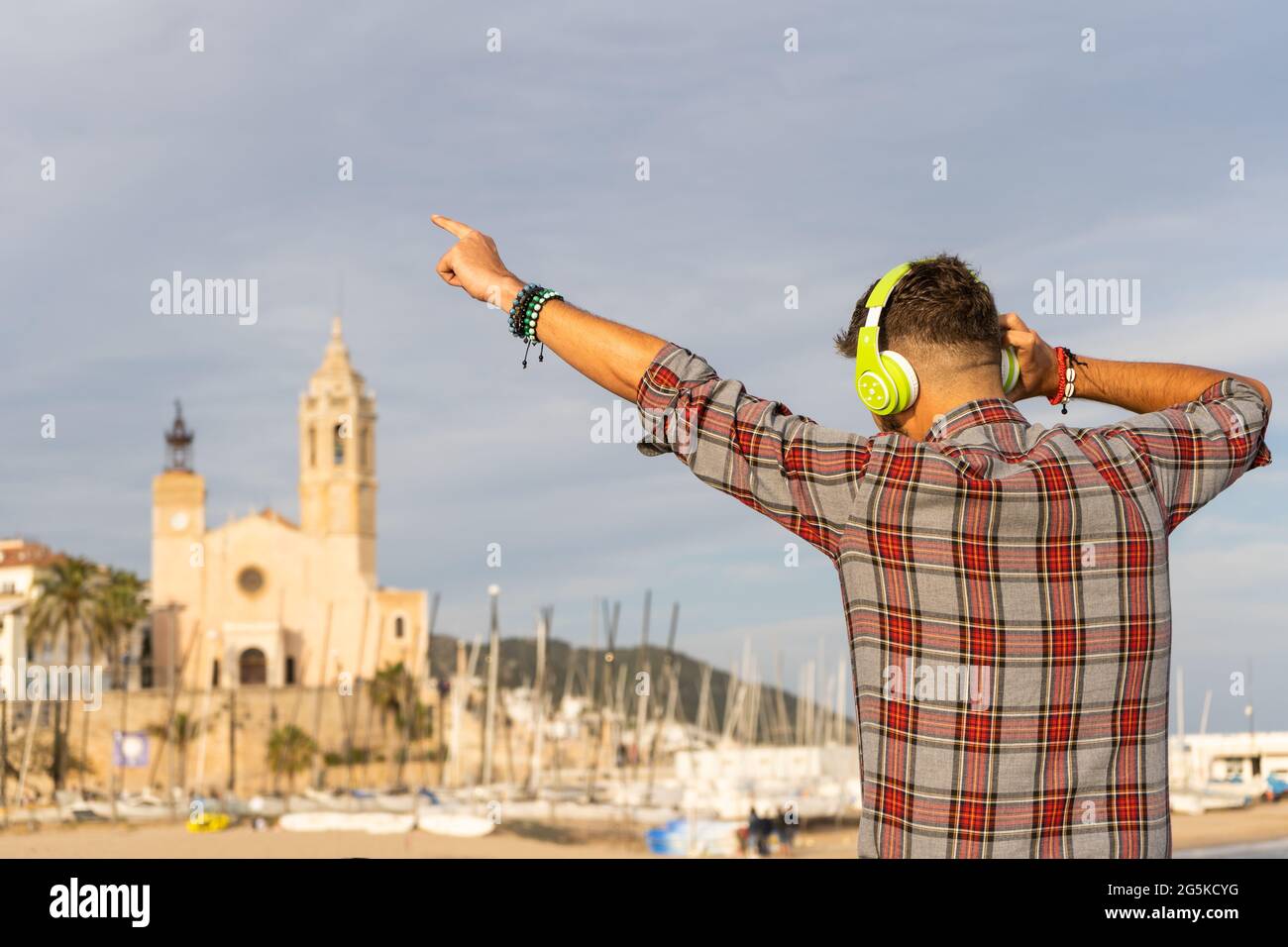 Felice uomo eccitato con alzando le braccia ascoltando musica con le cuffie sulla spiaggia. Foto Stock