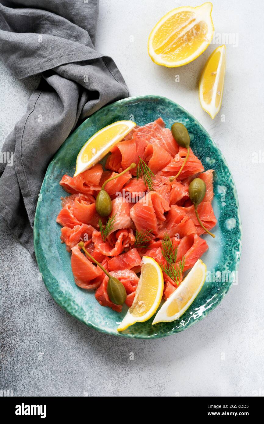 Fette di salmone salato con capperi, limone e aneto su un piatto di ceramica su fondo grigio di cemento. Vista dall'alto Foto Stock