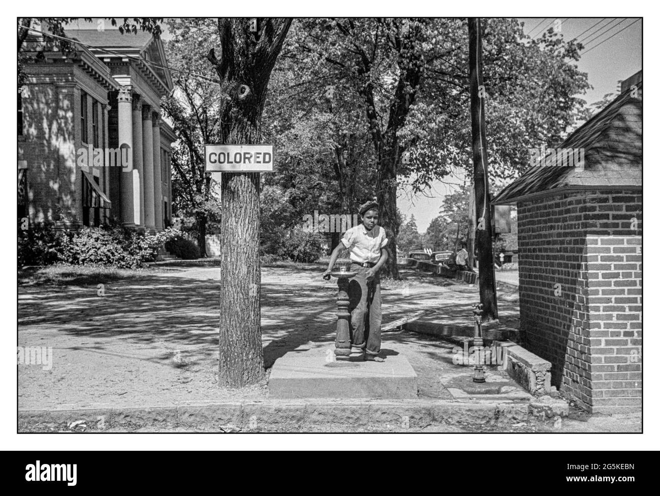 DISCRIMINAZIONE DELLA SEGREGAZIONE RAZZIALE USA con un cartello "colorato" sulla fontana per bere sul prato del tribunale della contea, con un giovane ragazzo afroamericano in piedi alla fontana. Halifax, North Carolina USA John Vachon fotografo 1938 . Foto Stock