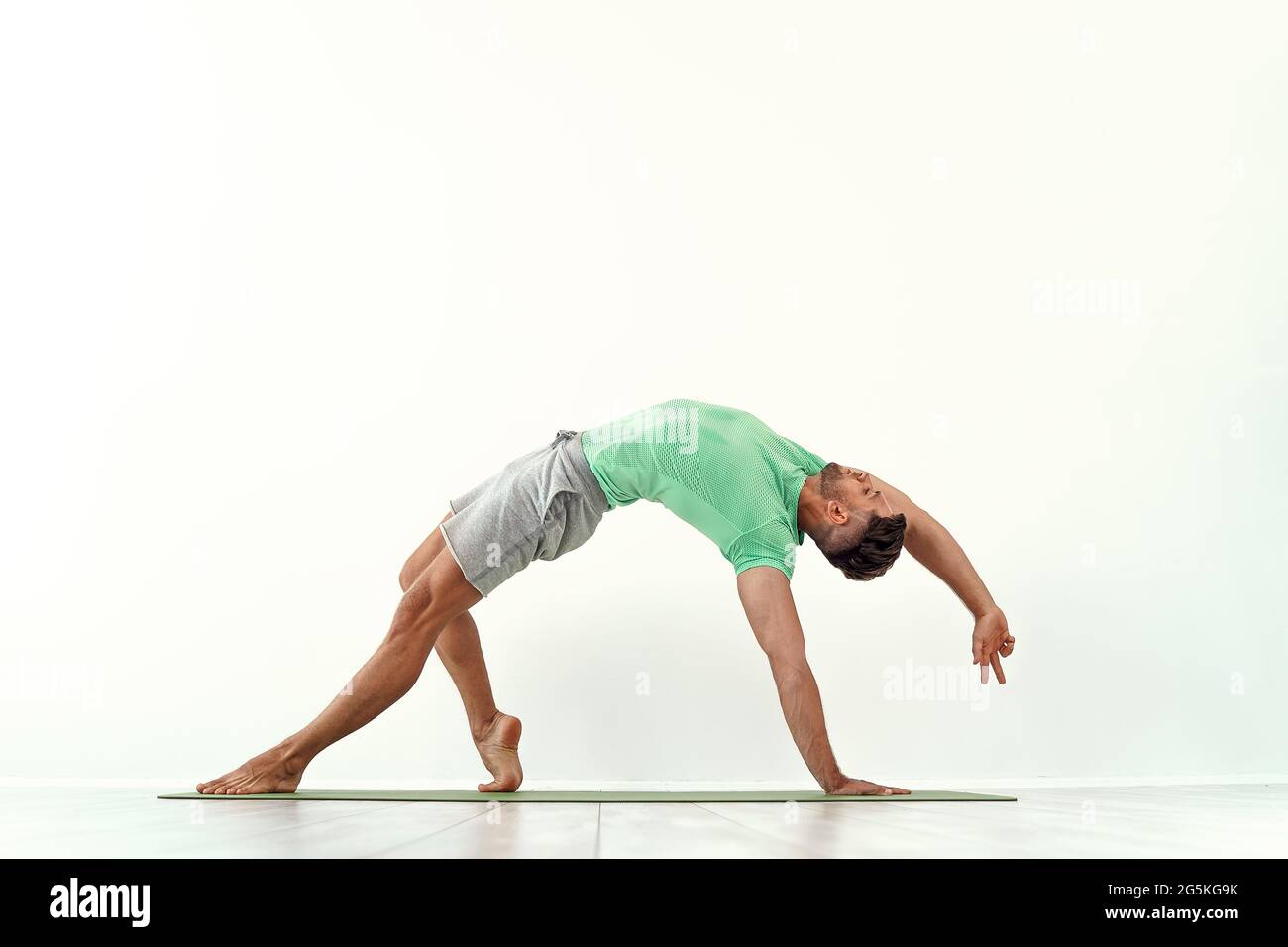 Fit maschile praticante yoga Wild Thing posa, Camatkarasana contro sfondo  bianco parete Foto stock - Alamy