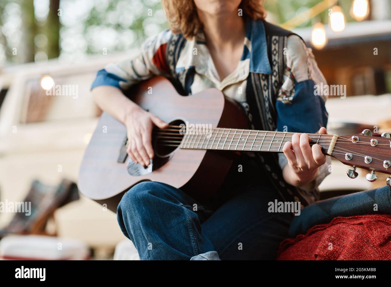 Primo piano di una giovane donna seduta sulla natura e suonando la chitarra Foto Stock