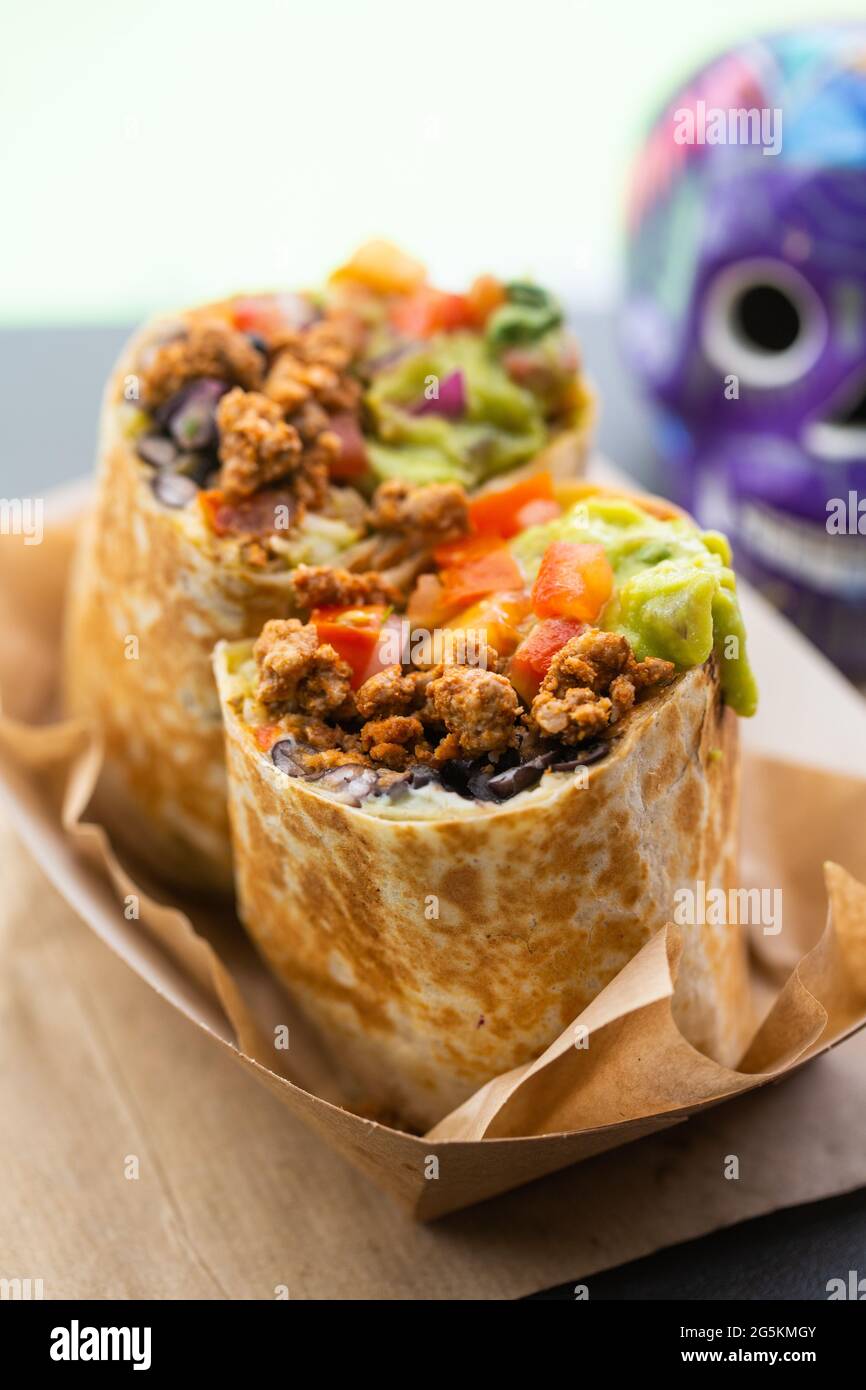 Burrito con carne tritata e salsa e guacamole in un fast food caffetteria di strada con un cranio sullo sfondo. Piatti messicani tradizionali Foto Stock