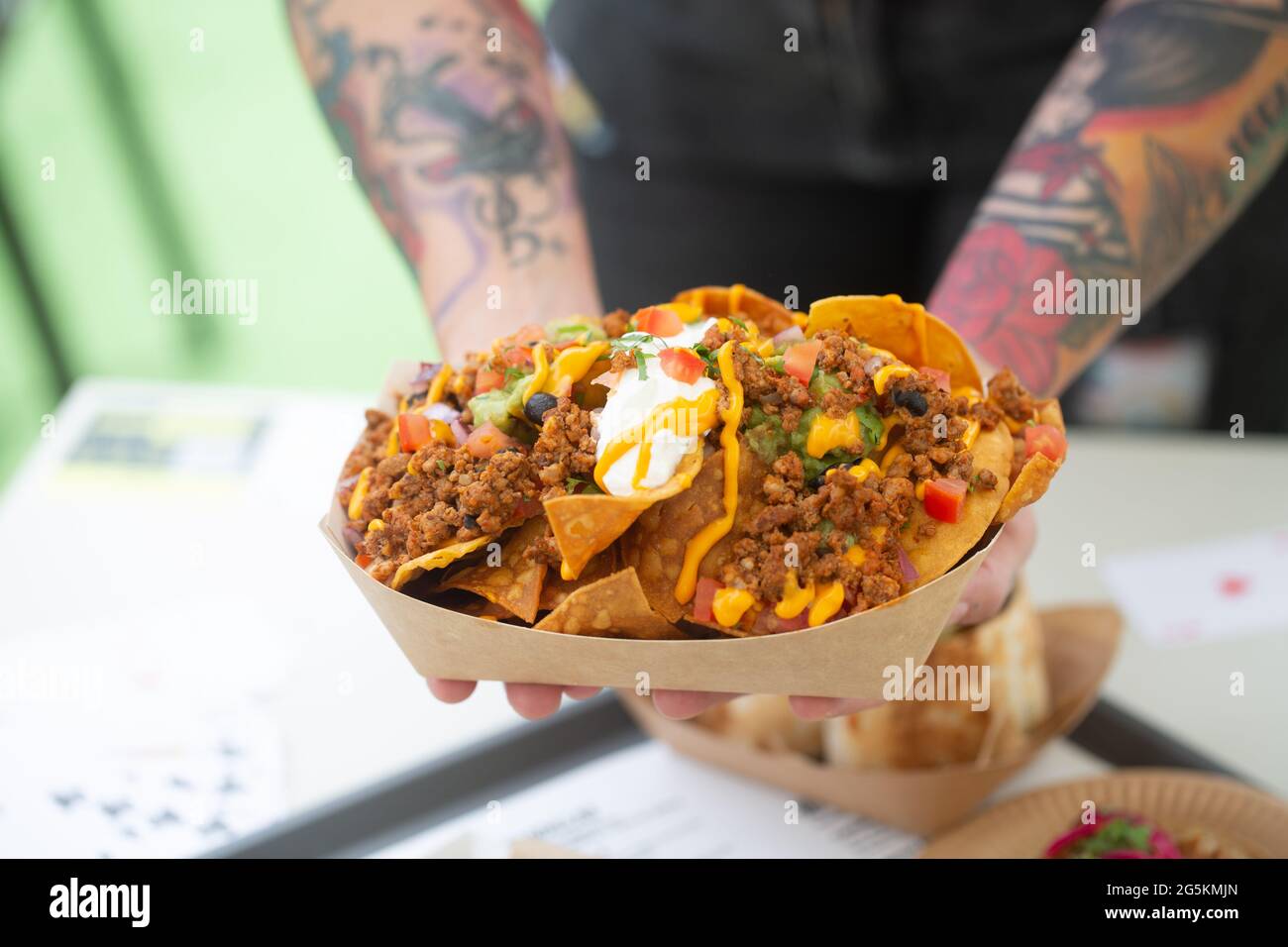 Lo chef di strada tatuato tiene la salsa nachos in un piatto di carta. Piatti messicani tradizionali Foto Stock