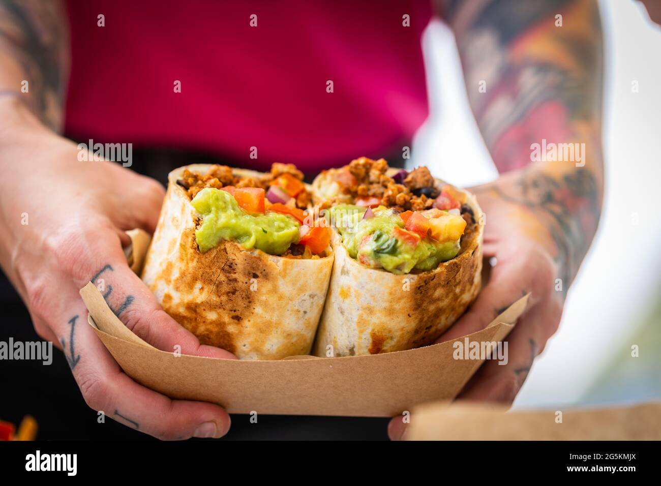 Le mani maschili di uno chef in un fast food café tengono un burrito con carne macinata, salsa e guacamole. Piatti messicani tradizionali Foto Stock