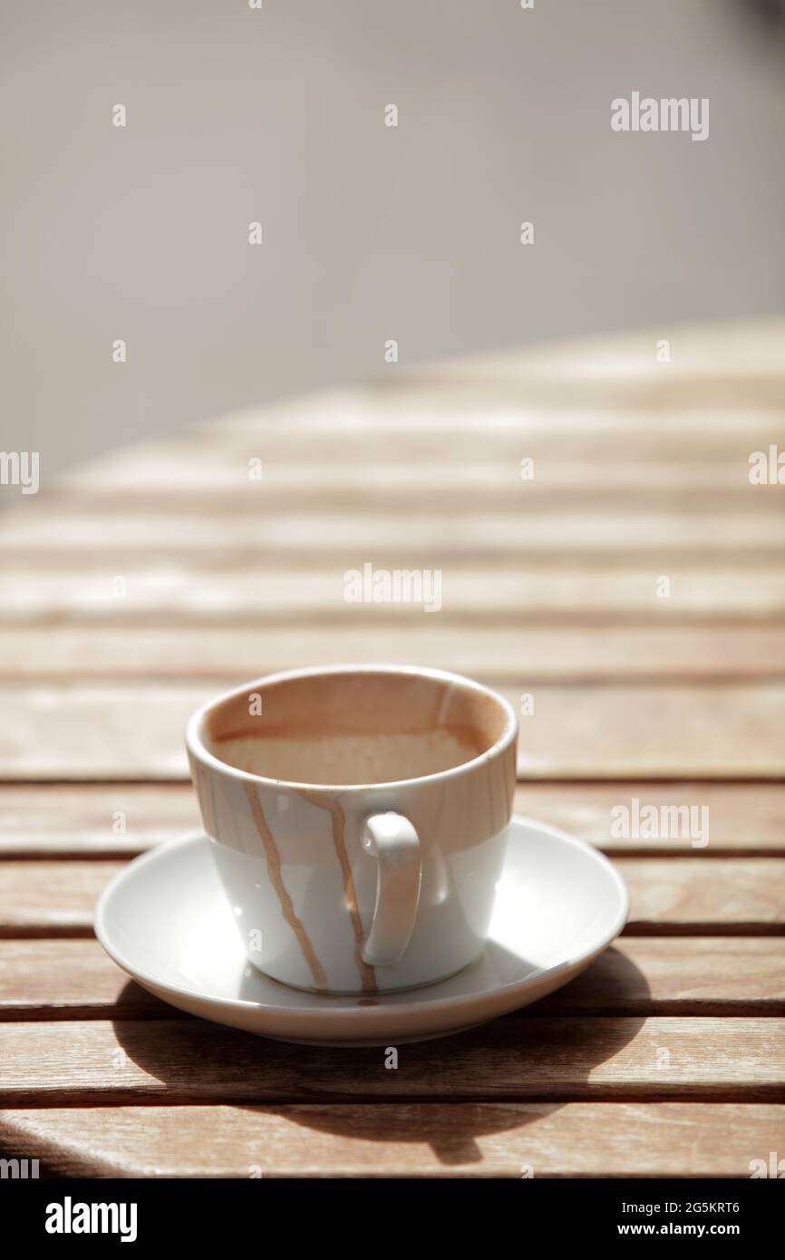 Una tazza vuota di caffè su un tavolo al sole Foto Stock