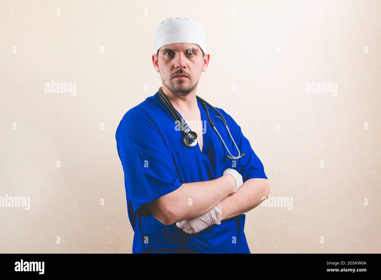 Giovane medico ritratto in tuta blu con stetoscopio e con le mani sul petto isolato su fondo liscio Foto Stock