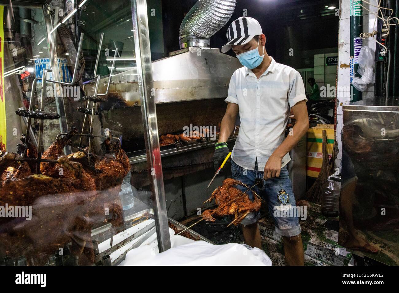 Street Food Cook rimuove il pollo arrosto dallo spiit da servire a Saigon Foto Stock