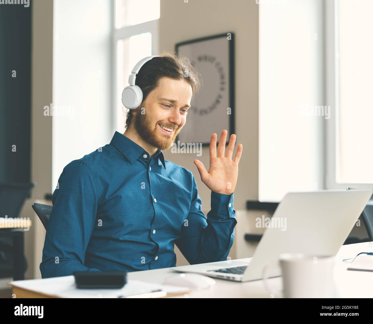 Giovane uomo felice lavoratore in ufficio con cuffie sorridenti durante la videochiamata Foto Stock