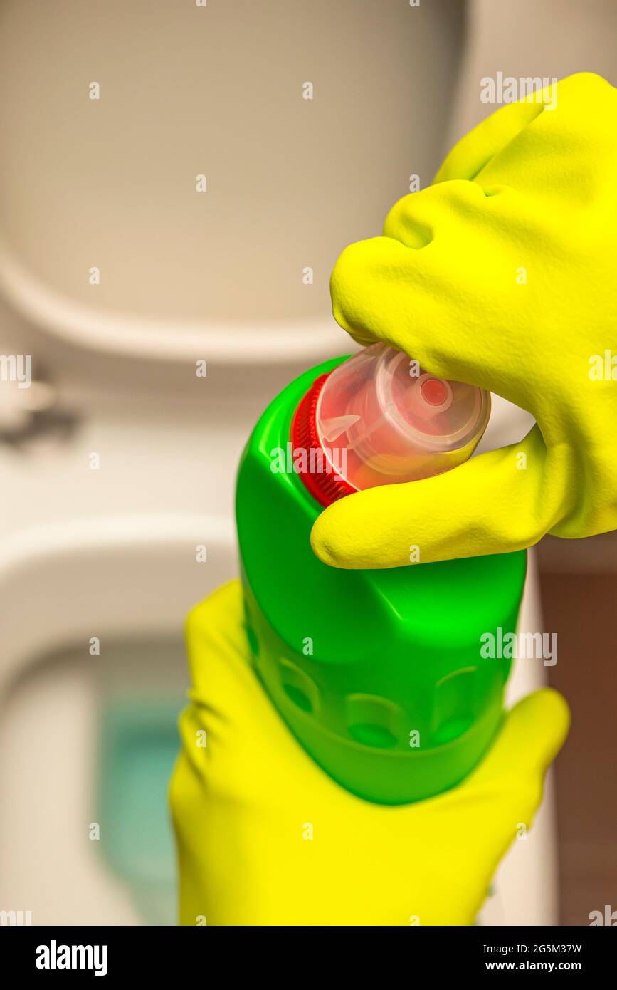 Pulizia e disinfezione dei servizi igienici. Aprire il detergente per wc prima dell'uso. Una mano con guanti pulisce il gabinetto con un disinfettante Foto Stock