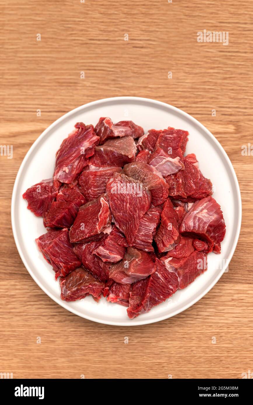 Cucinare pilaf in un calderone, una ricetta per il pilaf reale. Ingredienti per cucinare pilaf su fondo di legno. Carne cruda su un tagliere di legno, tagliata Foto Stock