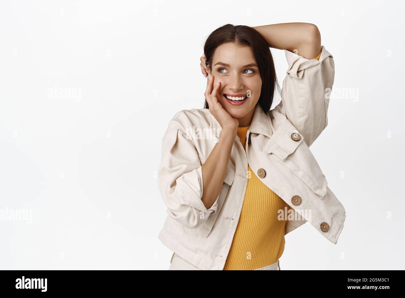 Donna tenera e femminile, ridendo coquetish, sorridendo denti bianchi, toccandoli i capelli e le guance, arrossendo il coy, guardando l'angolo in alto a sinistra Foto Stock