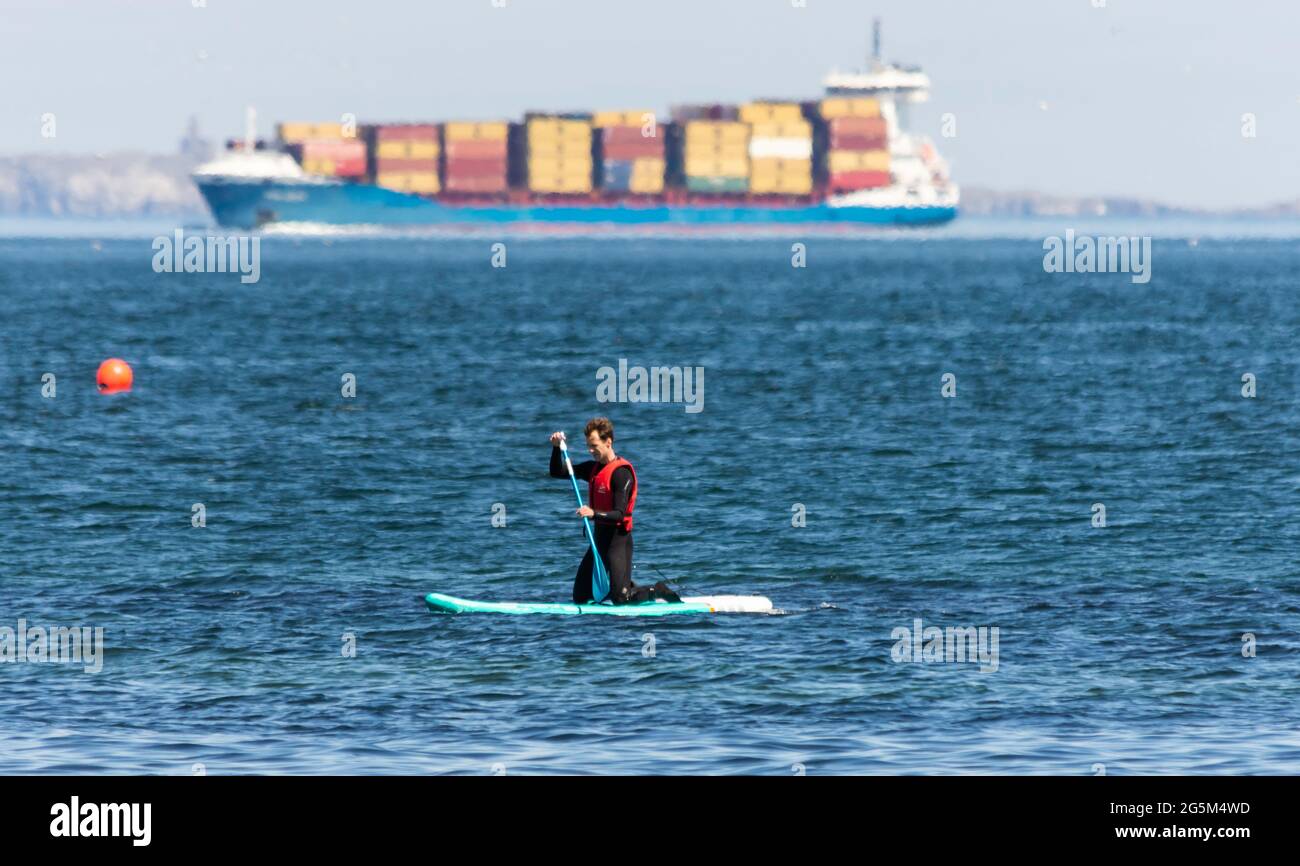 Un'ignota pagaia è salita a bordo delle pale nel firth of Forth, in Scozia, mentre un'enorme nave portacontainer passa sullo sfondo Foto Stock