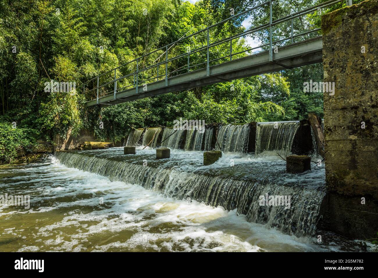 Cascata artificiale / Weir e passerella attraverso il fiume Claise vicino Mezieres-en-Brenne, Indre (36), Francia. Foto Stock