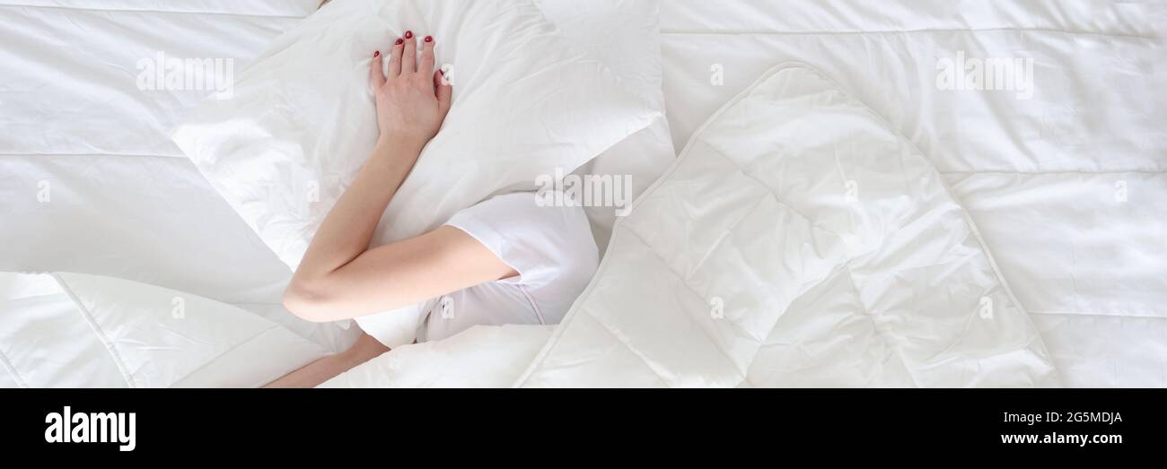 La donna sotto le coperture ha coperto la sua testa con la vista del cuscino superiore Foto Stock