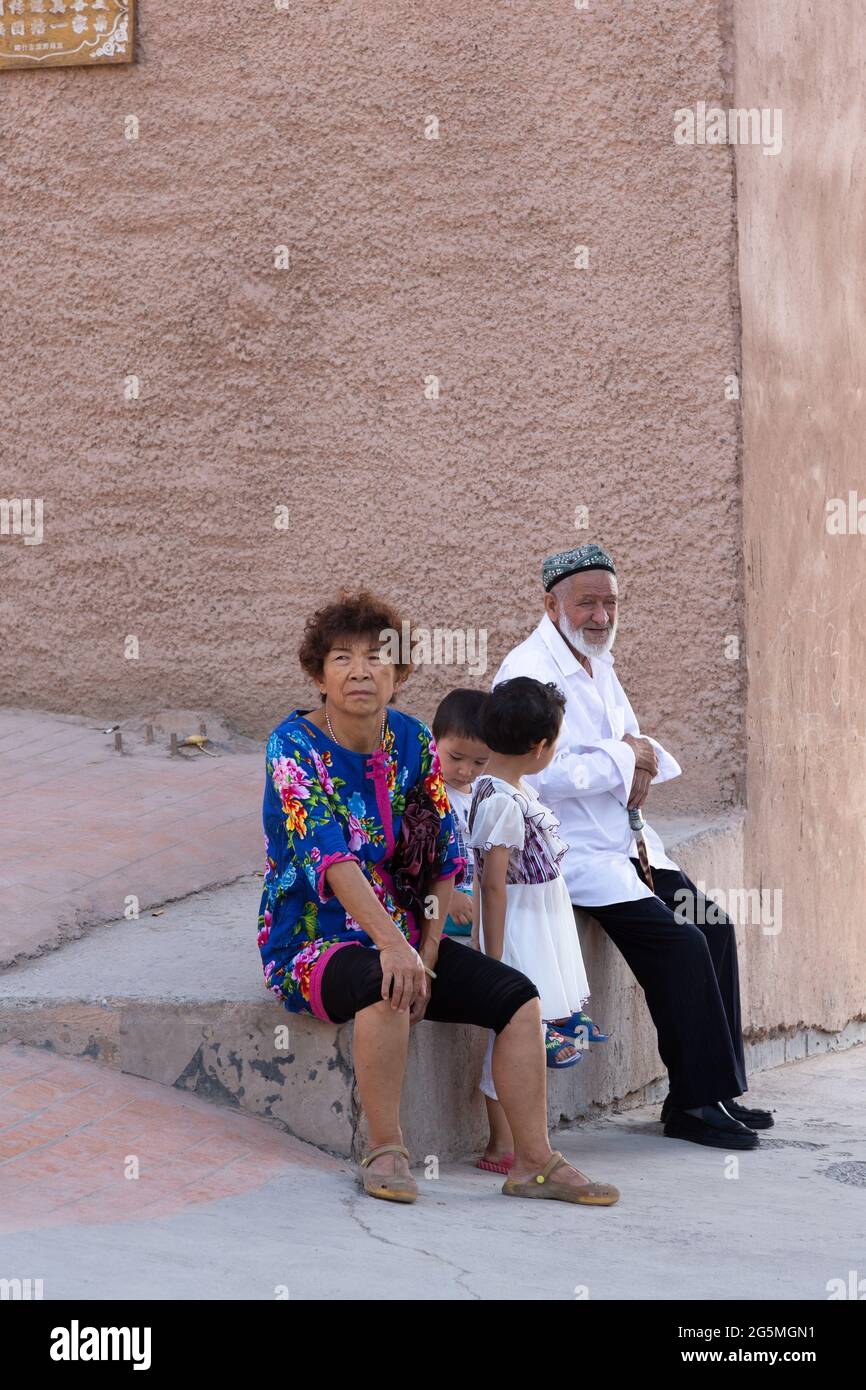 I nonni siedono con i loro due nipoti su un muro all'ombra Foto Stock