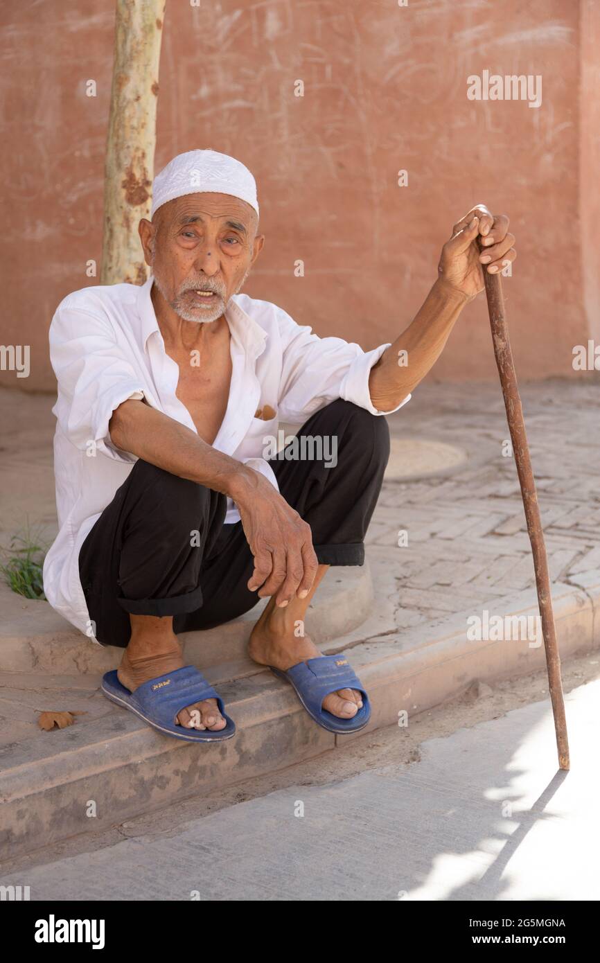 Un uomo anziano con una canna si siede su un gradino di fronte ad un albero Foto Stock