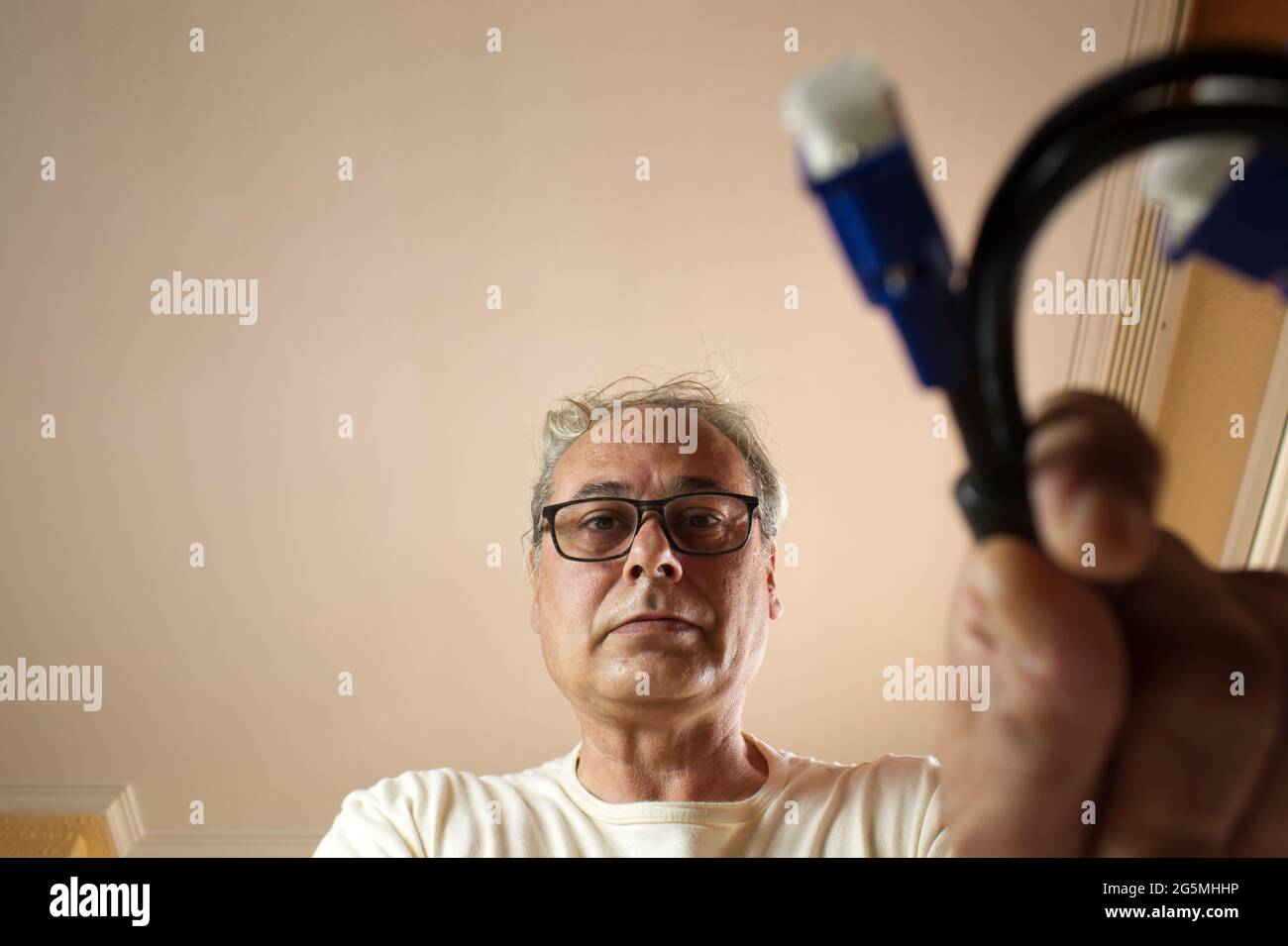 uomo maturo con capelli grigi che prende un cavo da un cassetto a casa Foto Stock
