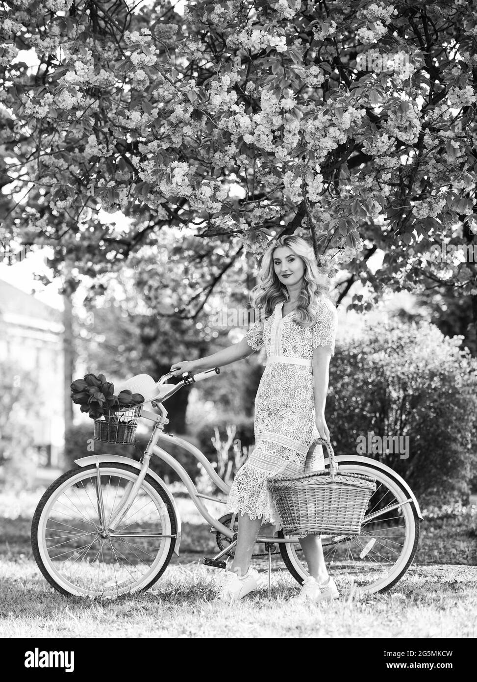 Estate fantastica. Viaggi. Donna retrò vendere bouquet di fiori di tulipano. Ragazza sotto sakura con bicicletta d'epoca. Bellezza primaverile e moda. Rosa ciliegia Foto Stock