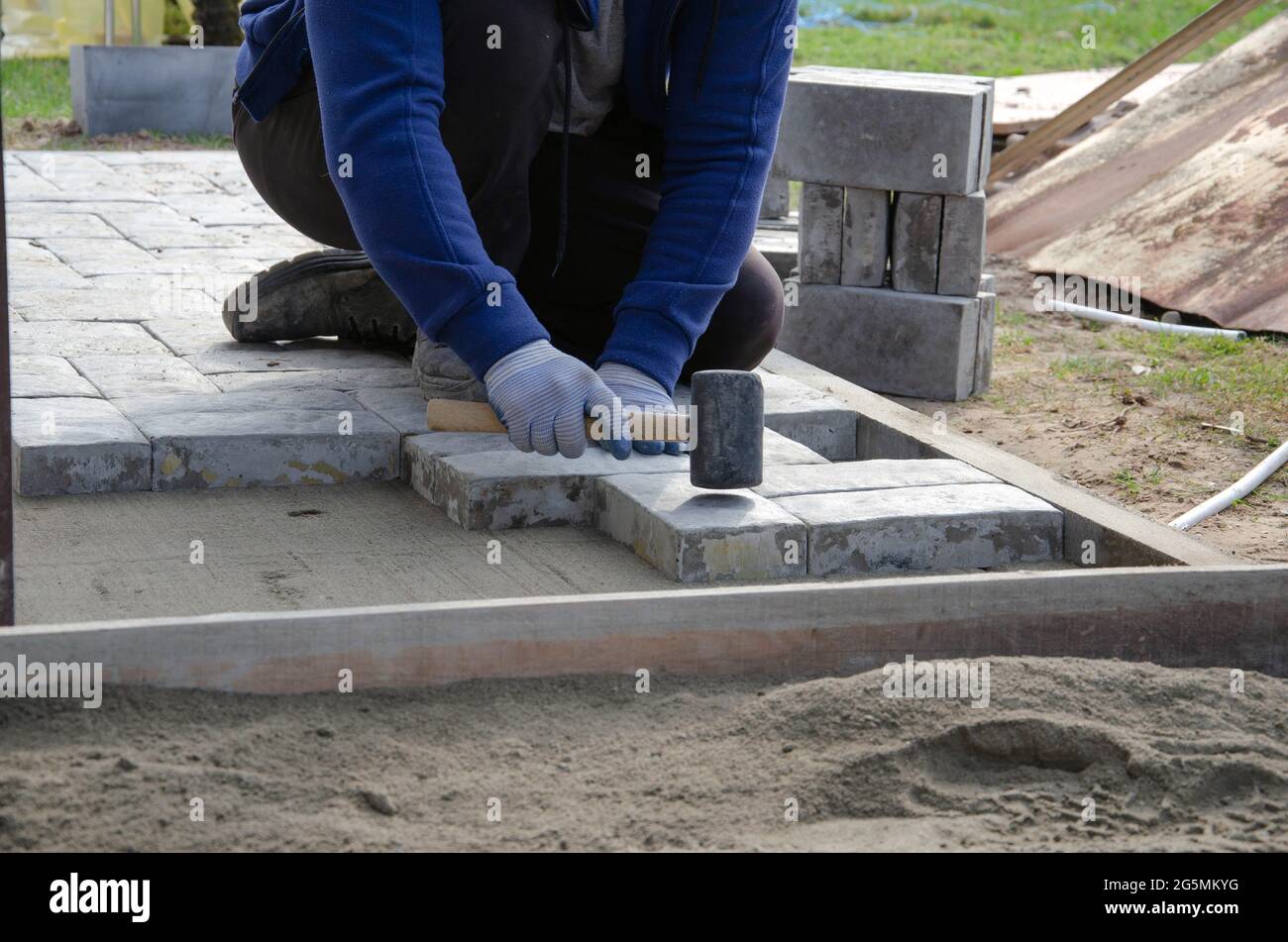 Costruzione di pavimentazione vicino alla casa. Muratore posiziona blocchi di pietra di pavimentazione di calcestruzzo per costruire su un Foto Stock