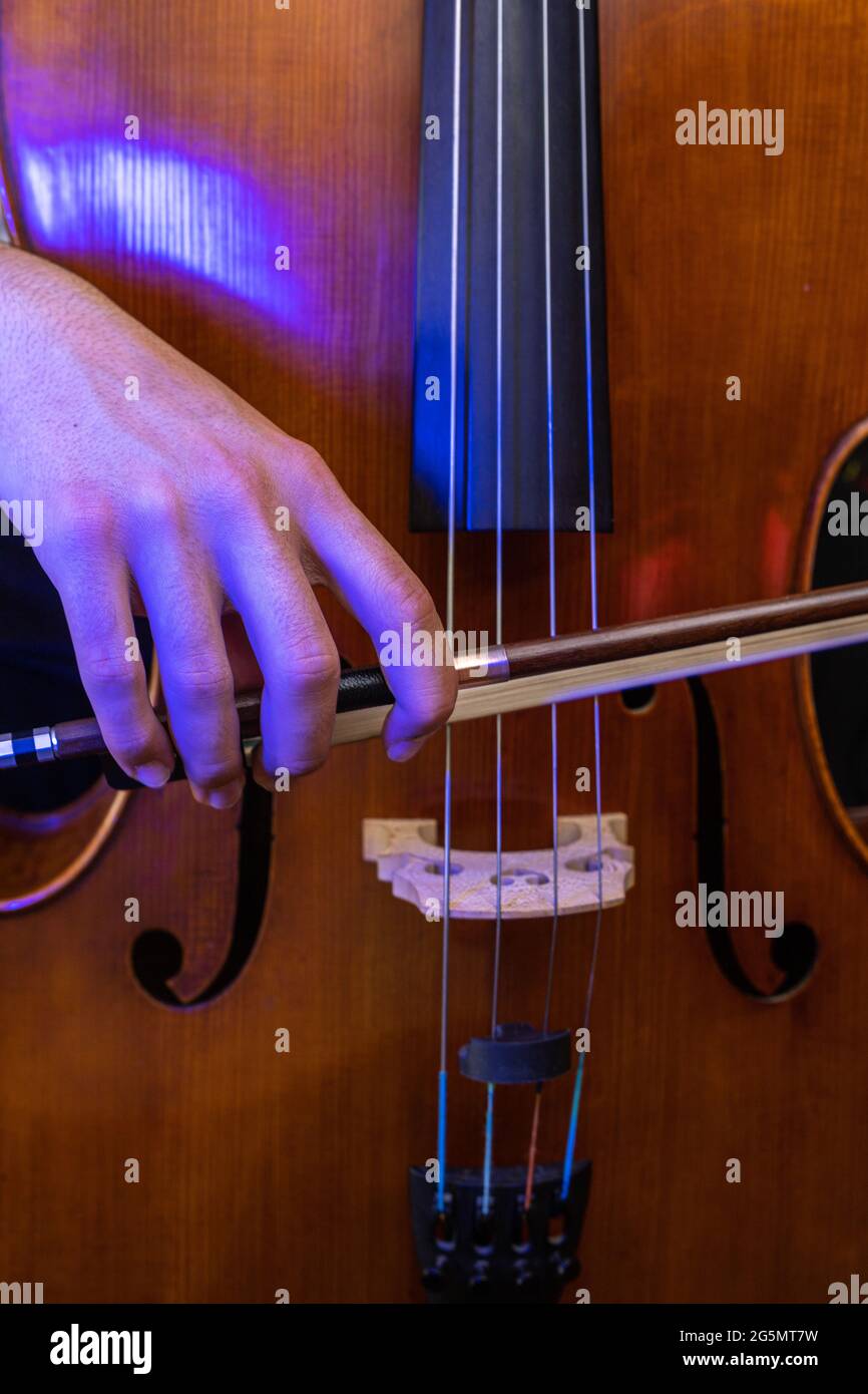 violoncello in legno con luce blu e mano con un archetto musicale che strumica le corde per suonare una canzone con messa a fuoco selettiva Foto Stock